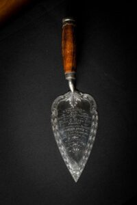 An inscribed metal trowel on a black surface. The inscription reads